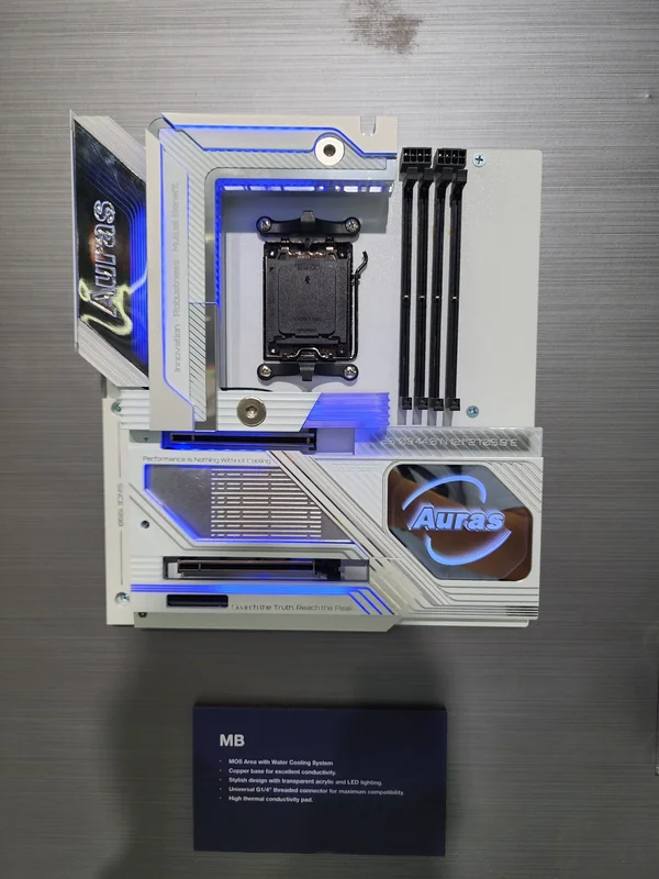A white and blue Auras motherboard with LED lighting and the text 'Performance is Nothing Without Cooling' is displayed vertically with dimm slots and a CPU socket visible.
