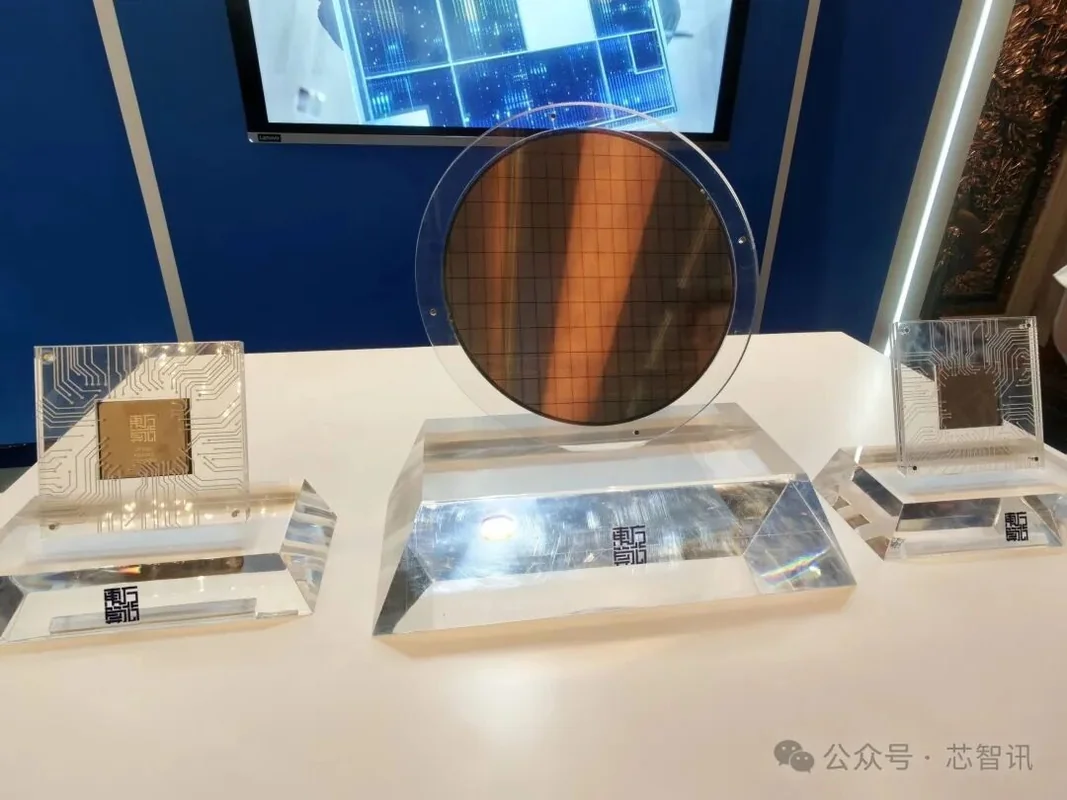 A display featuring a silicon wafer and two semiconductor chips encased in transparent blocks, with circuitry patterns visible on a table in an exhibition setting.