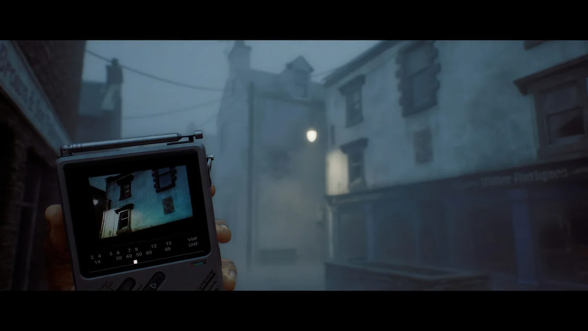 A hand holding a Tera-650b portable television displaying an image of a building on a foggy street at night.