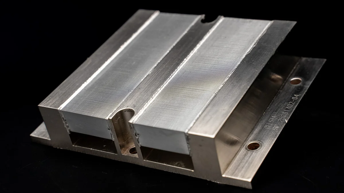 A close-up view of an unbranded metallic heat sink with grooved fins and visible engraving on its side.