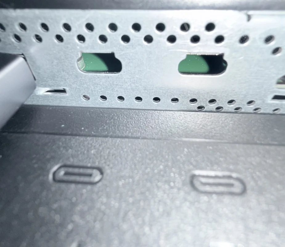 A close-up of a metal panel with ventilation holes and visible USB-C port markings on a piece of hardware.