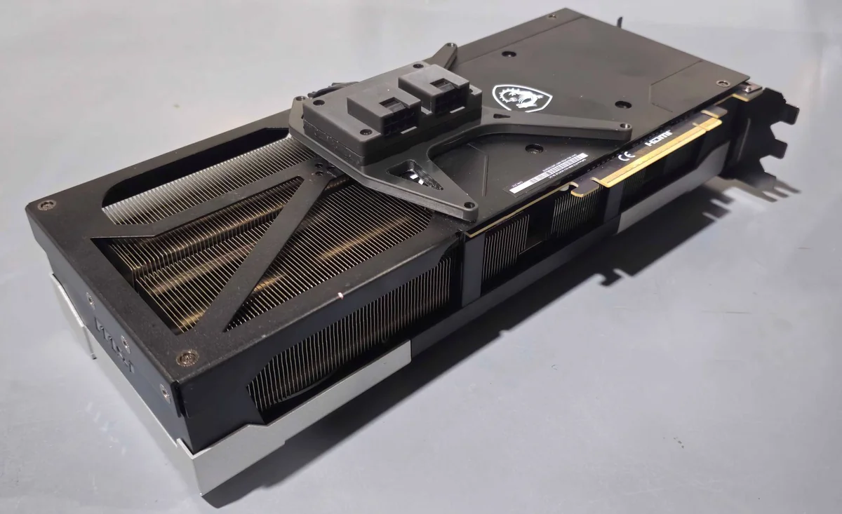 An MSI graphics card with a visible cooling system and dual 8-pin power connectors is placed on a gray surface.